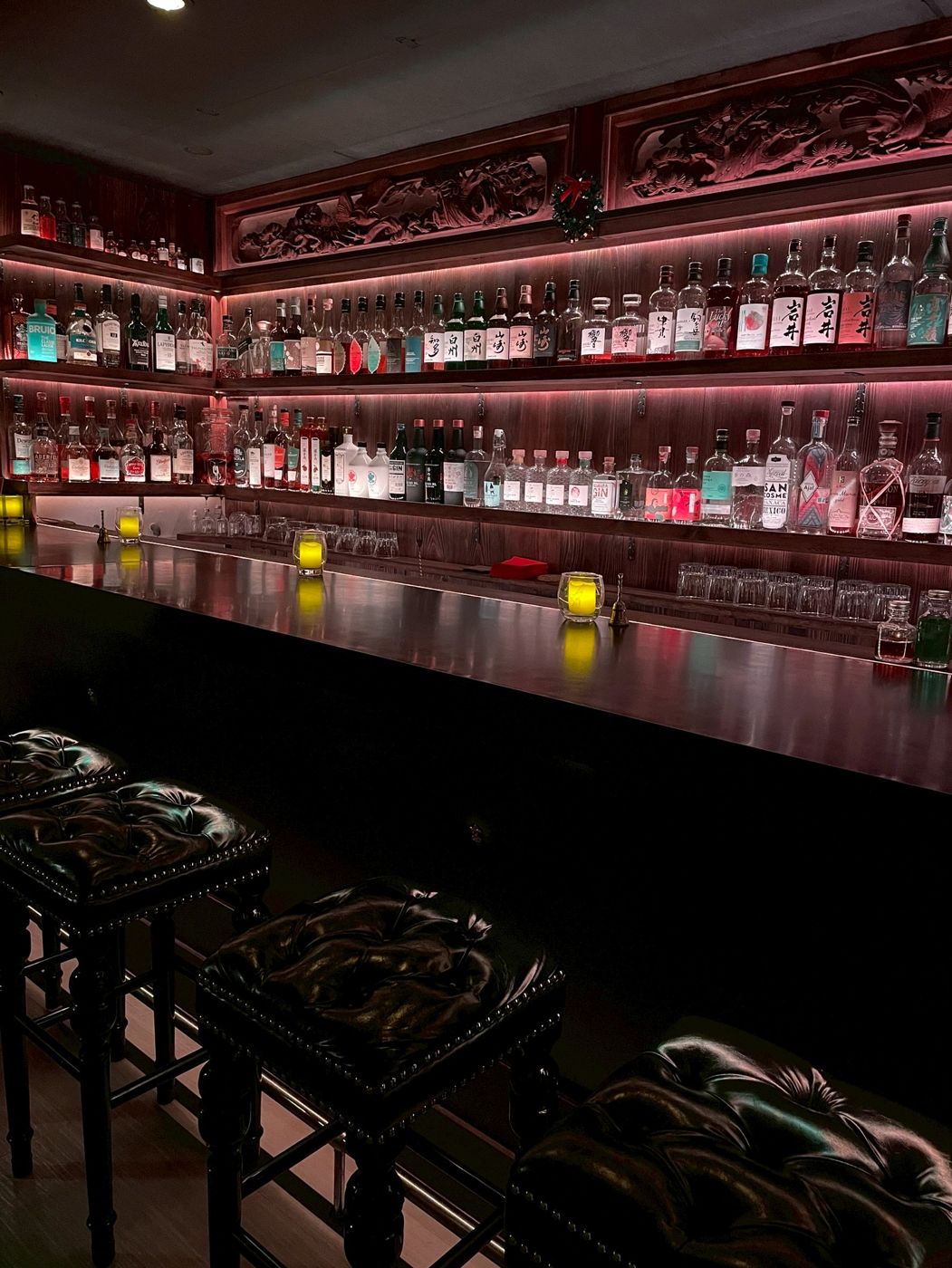 The back bar at Frontier Bar Kyoto, lit in red, with Japanese whisky bottles under a carved wooden ranma of pine and hawk