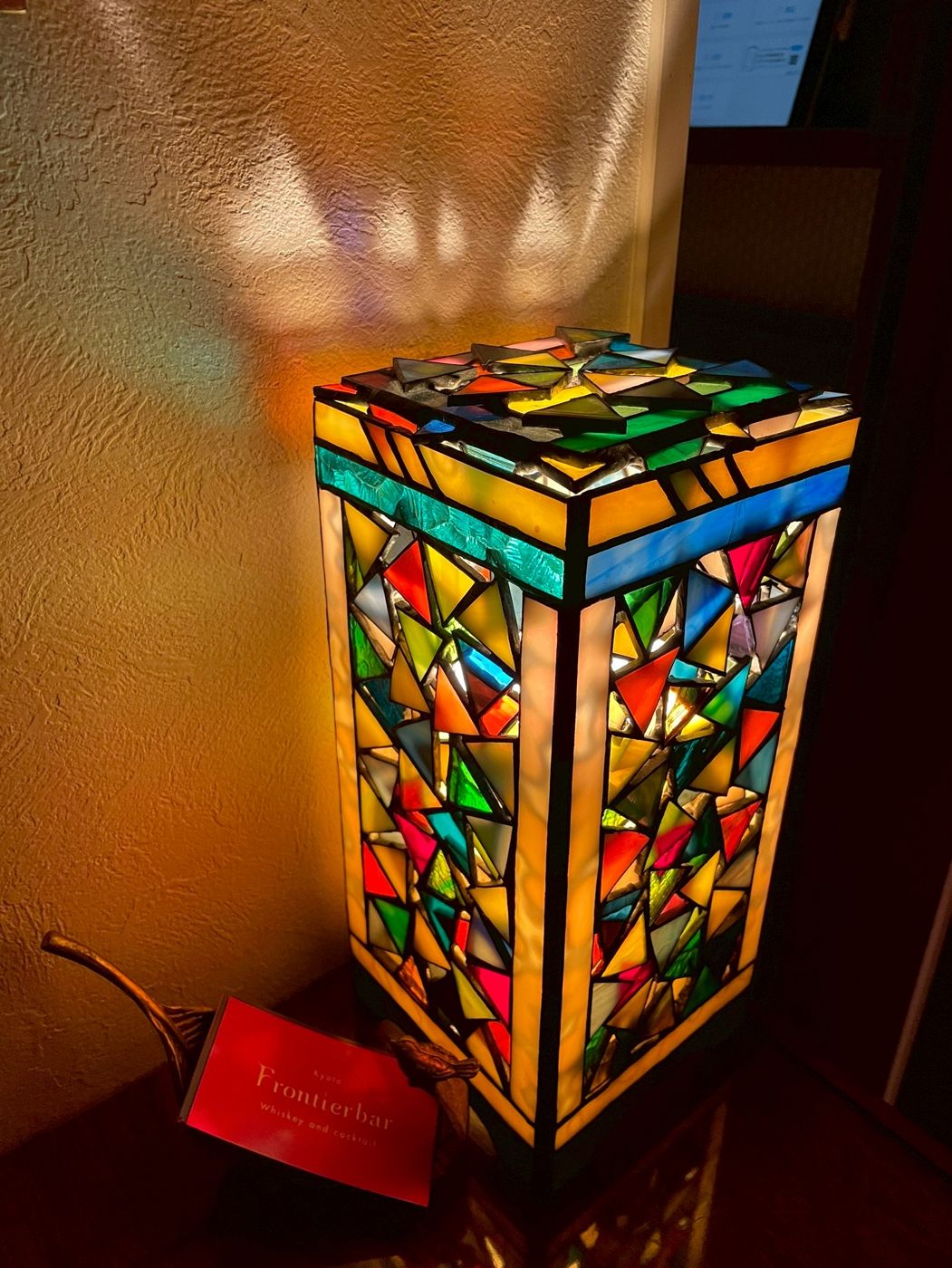 A glowing stained glass lamp next to a red Frontier bar card