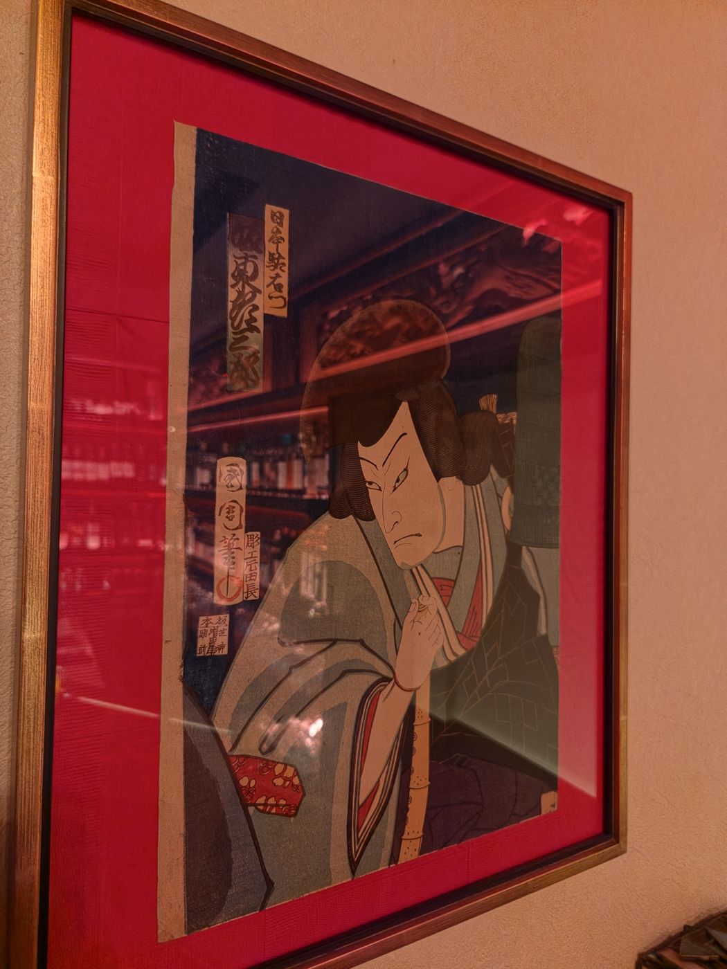A framed ukiyo-e woodblock print of a kabuki actor on a red mat